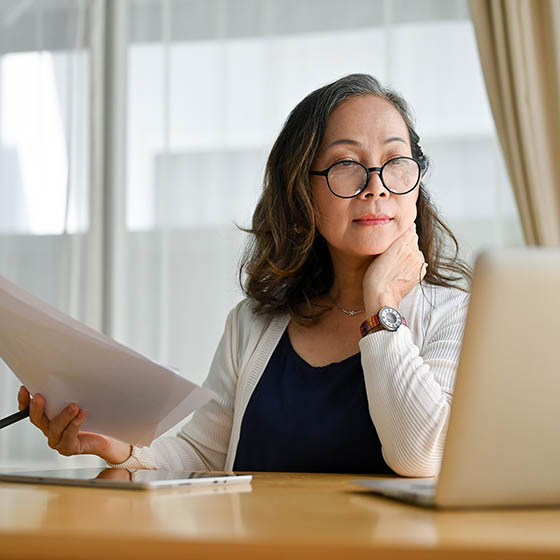 Woman looking at laptop while holding papers